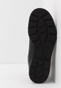 Bota preta de couro com uma sola texturizada. Padrão de ranhura notável para tração, com a marca visível na sola. Lados lisos e bico arredondado.