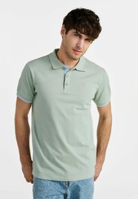 Jasnozielona koszulka polo z klasycznym kołnierzykiem, z niebieskim akcentem na plisie i rękawach, wykonana z teksturowanej tkaniny z małym logo.
