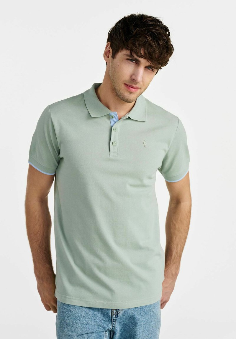 Jasnozielona koszulka polo z klasycznym kołnierzykiem, z niebieskim akcentem na plisie i rękawach, wykonana z teksturowanej tkaniny z małym logo.