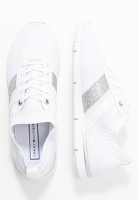 Vita atletiska sneakers med ett andningsbart stickat överdel, silverglitter och solida vita ränder, med en texturerad sula och snörningsdesign.