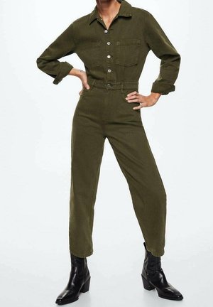 Olivi vihreä haalari, jossa on pitkät hihat, kaksi rintataskua, hopeiset napit ja kapenevat lahkeet; yhdistetty mustiin nilkkasaappaisiin.