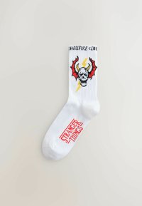 Hvid kort strømpe med farverigt motiv af en kranium med horn, røde vinger og lyn. Rød "Stranger Things"-tekst nær tåen.
