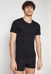 T-shirt noir à manches courtes en mélange de coton, avec un col rond et une coupe ajustée. Porté avec un short boxer noir.