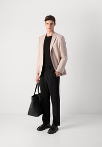 Svetlo béžový kockovaný blazer cez čierny top, doplnený voľnými čiernymi nohavicami. Čierne topánky a čierna kabelka dokončujú outfit.