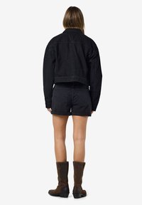 Black cropped denim jacket with long sleeves, paired with black shorts and knee-high brown leather boots. Smooth texture and simple design.