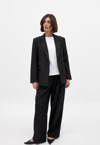 Melnā pielāgotā bleizeris ar divām pogām, uzvilkts virs balta T-krekla. Saskaņots ar augsto vidukli melnām platām biksēm un melnām norādītām kurpēm.