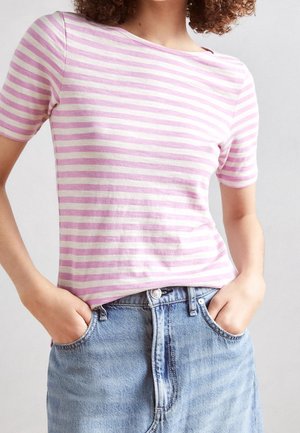 Woman wearing a short-sleeve pink and white striped top tucked into a light blue denim skirt, with hands in pockets.