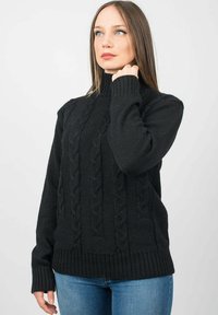 Pullover nero in maglia con collo alto, caratterizzato da un motivo a treccia e polsini e orlo a costine. Indossato sopra jeans blu.