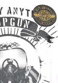 Svartvit grafik som visar en pilots ansikte i hjälm. "TOP GUN" text och en broderad cirkulär patch med vingar och tre stjärnor.