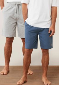 Graue und blaue Shorts mit elastischem Bund, Seitentaschen und einem kleinen Logo auf der blauen Variante, vor einem Holzfußboden-Hintergrund.
