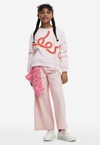 Vaaleanpunainen collegepaita, jossa on värikäs kiertokuvio, yhdistetty vaaleanpunaisiin leveälahkeisiin housuihin ja vaaleanpunaiseen kuvioituun huiviin, puettuna valkoisten tennareiden kanssa.