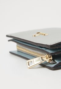 Portafoglio compatto in pelle grigia texturizzata, con interno blu, zip e hardware dorati. Presenta un design sovrapposto per un facile accesso ai contenuti.