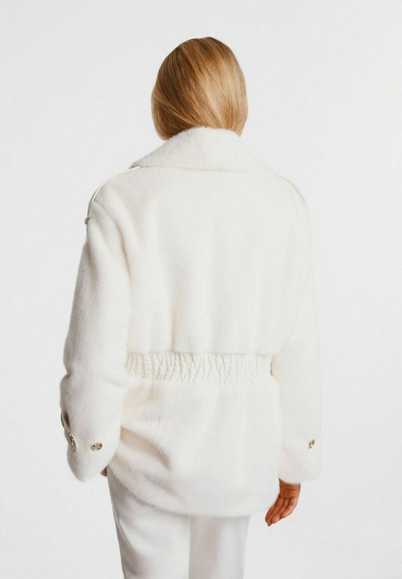 Biała polarowa kurtka z kołnierzykiem, elastycznym pasem i zapinanymi rękawami. Miękka tekstura, prosta forma i czyste linie.