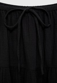 Tissu noir tissé avec une finition texturée. Doté d'un cordon de serrage à la taille et de coutures froncées, créant une apparence superposée.