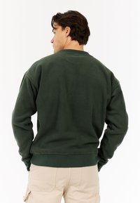 Donkergroene fleece sweatshirt met een ronde halslijn en ribgebreide manchetten, met een gladde textuur en een losse pasvorm.