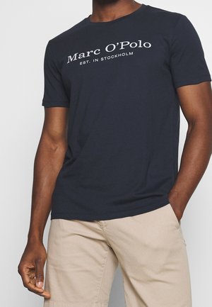 T-shirt en coton bleu marine avec col rond et manches courtes, portant l'inscription "Marc O'Polo EST. IN STOCKHOLM" en texte blanc.