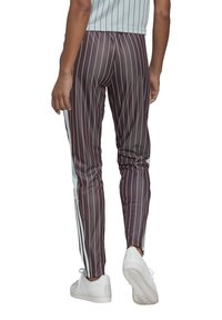 Pantalons rayés marron avec une texture brillante, présentant des panneaux latéraux blancs et une coupe slim. Portés avec des baskets blanches.