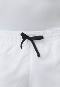 Bañadores blancos con cordón negro, cinturilla elástica, textura suave y sin patrones ni logos visibles.