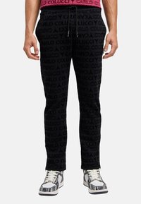 Sorte sweatpants med et struktureret mønster, der har gentaget branding. Bukserne har en snor i taljen og er parret med mønstrede sneakers.