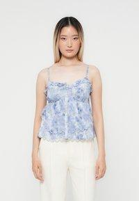 Lichtblauw bloemenpatroon top met ruffles, verstelbare bandjes en knopen aan de voorkant. Zachte, doorschijnende stof met een golvende zoomafwerking.
