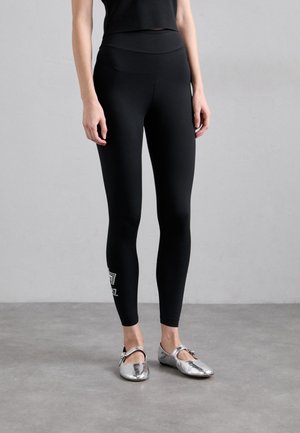 Zwarte leggings met een gladde textuur, aansluitend ontwerp en enkel lengte. Voorzien van een wit logodetail nabij de zoom. Gecombineerd met glanzende zilveren flats.