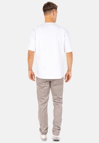Witte T-shirt met korte mouwen gecombineerd met lichtgrijze textuur broek, voorzien van twee achterzakken en een recht gesneden ontwerp, met witte sneakers.