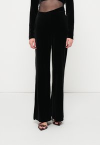 Μαύρο βελούδινο παντελόνι με φάρδος, με ομαλή υφή, που διαθέτει ψηλή μέση και κομψό, ραμμένο σχέδιο. Φοριέται με μαύρες ψάθινες γόβες.