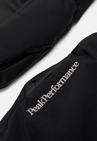 Veste de sport noire avec une texture lisse, des épaules rembourrées et "PeakPerformance" brodé en argent sur la manche.