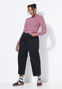 Camisa de lana a rayas de manga larga en burdeos y blanco, pantalones negros de talle alto, y zapatillas burdeos con detalles en blanco y calcetines a rayas.