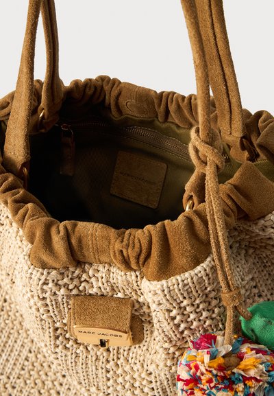 Μπεζ υφασμάτινη τσάντα Marc Jacobs με καφέ σουέτ διακοσμητικές λεπτομέρειες, κλείσιμο με κορδόνι, εσωτερική τσέπη με φερμουάρ και πολύχρωμο μπρελόκ με πομ-πομ.