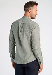 Camisa de manga larga en tejido texturizado de color verde claro. Presenta un cuello alzado, puños abotonados y un pliegue en la parte posterior para mayor movilidad.