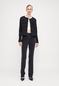 Black denim jacket with button-up front and two chest pockets, paired with matching black straight-leg jeans and a white cropped top.