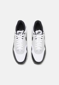 Nike Air Max sneakers featuring a white mesh upper, gray accents, black rubber sole, and white laces, with a logo on the tongue.