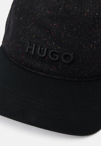 Sort kasket med en spraglet tekstur, prydet med et præget "HUGO" logo på fronten. Blødt stof med en buet skygge.