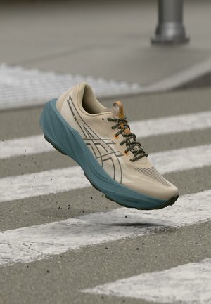 Chaussure de course beige et bleue avec lacets noirs capturée en plein air au-dessus d'un passage piéton avec des particules de gravier en suspension.