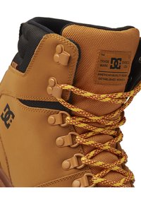 Bottes d'extérieur en cuir marron avec un col en tissu texturé, lacets à motifs jaunes et rouges, et matériel en métal ; présente le logo de la marque sur le côté.