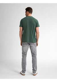 Zelené bavlněné tričko s krátkými rukávy a kulatým výstřihem, doplněné světle šedými džínami s vybledlou texturou a našitými zadními kapsami.