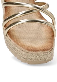 Tiras metálicas doradas en espiral en una sandalia de plataforma. Suela beige texturizada con acentos de yute trenzado y una plantilla suave y lisa.