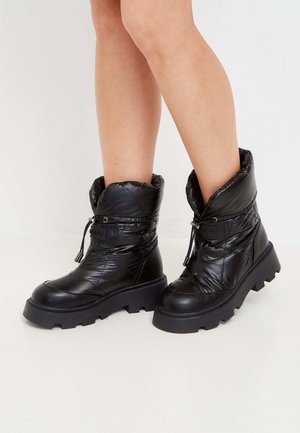 Jambes portant des bottes d'hiver noires épaisses avec des semelles épaisses et des empeignes matelassées et rembourrées serrées par des cordons de serrage.