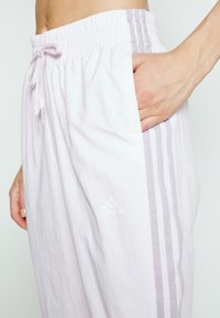 Ljust rosa träningsbyxor med en rynkad elastisk midja, dragsko och tre kontrasterande vertikala ränder längs sidorna.