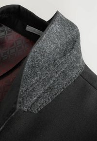 Czarny garment z szarym filcowym kołnierzem. Wnętrze wykończone wzorzystą czerwoną podszewką. Tekstura tkaniny jest gładka i strukturalna.