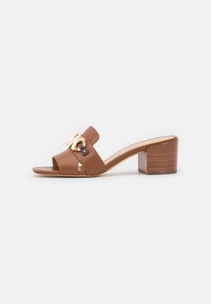 Mule sandale marron à bout ouvert avec un talon bloc et une boucle décorative en métal doré sur la bride supérieure en cuir.
