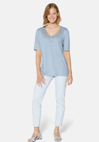 Lichtblauwe top met korte mouwen en kantafwerking bij de V-hals, gecombineerd met lichtgebloemde broek en lichtblauwe sandalen.