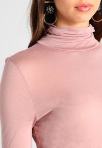 Rosa polotröja i mjukt, stretchigt tyg. Har en figurnära silhuett med rynkat mönster vid kragen och slät yta.