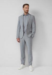 Grau Anzug mit Revers, kombiniert mit einem hellen Karohemd. Weiße Sneaker runden das Outfit ab und setzen einen modernen Kontrast im Stil.