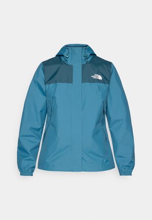 Waterproof jacket in teal with dark blue shoulder panels, zippered side pockets, elastic cuffs, and adjustable hood. Features logo on chest.
