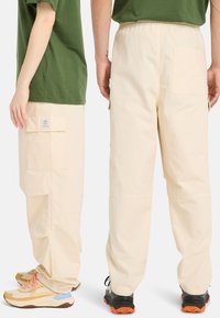 Ljusbeige cargobyxor med sidofickor och elastisk midja, som bärs med grön t-shirt och flerfärgade sneakers. Texturerad tyg, avslappnad passform.