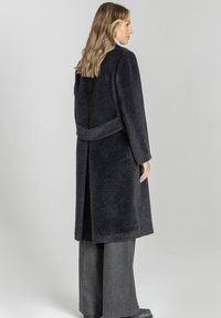 Ciemnoszary płaszcz z polaru z paskiem w talii, długimi rękawami i długością do połowy łydki, charakteryzujący się miękką fakturą i klasycznym krojem.