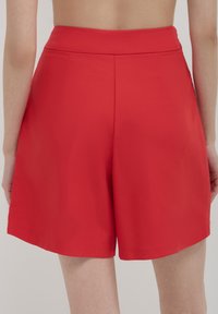 Vue arrière d'une personne portant un short rouge taille haute en tissu lisse et propre, sans poches ni motifs visibles.