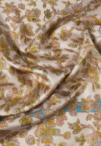 Υφάσμα κρεμ με πολύχρωμο λουλουδάτο σχέδιο σε πράσινο, ροζ, μπλε και κίτρινο, απαλά διπλωμένο που δείχνει υφή και λεπτομέρειες.